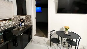 A compact kitchen with a dining area, a flat-screen TV mounted on the wall, and a small table with chairs. - Miami Gardens Comfort Suite by Hard Rock Stadium (Miami Gardens)