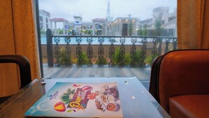 A table with a menu in a restaurant with a view of buildings and a railing. - Moon Star Beach Resort (Kanthi)