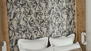Une chambre à coucher avec un grand lit, des oreillers blancs et beiges, et un mur à motifs derrière le lit.