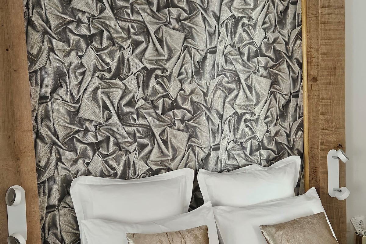 A bedroom with a large bed, white and beige pillows, and a textured wall behind the bed.