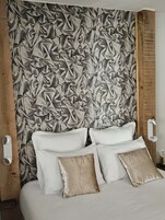 Un dormitorio con una cama grande, almohadas blancas y beige, y una pared texturizada detrás de la cama.