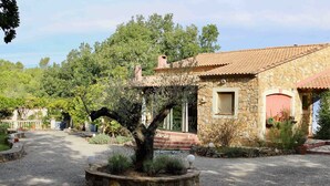 Une maison en pierre avec un toit en tuiles, entourée d’arbres et bordée d’une allée en gravier.