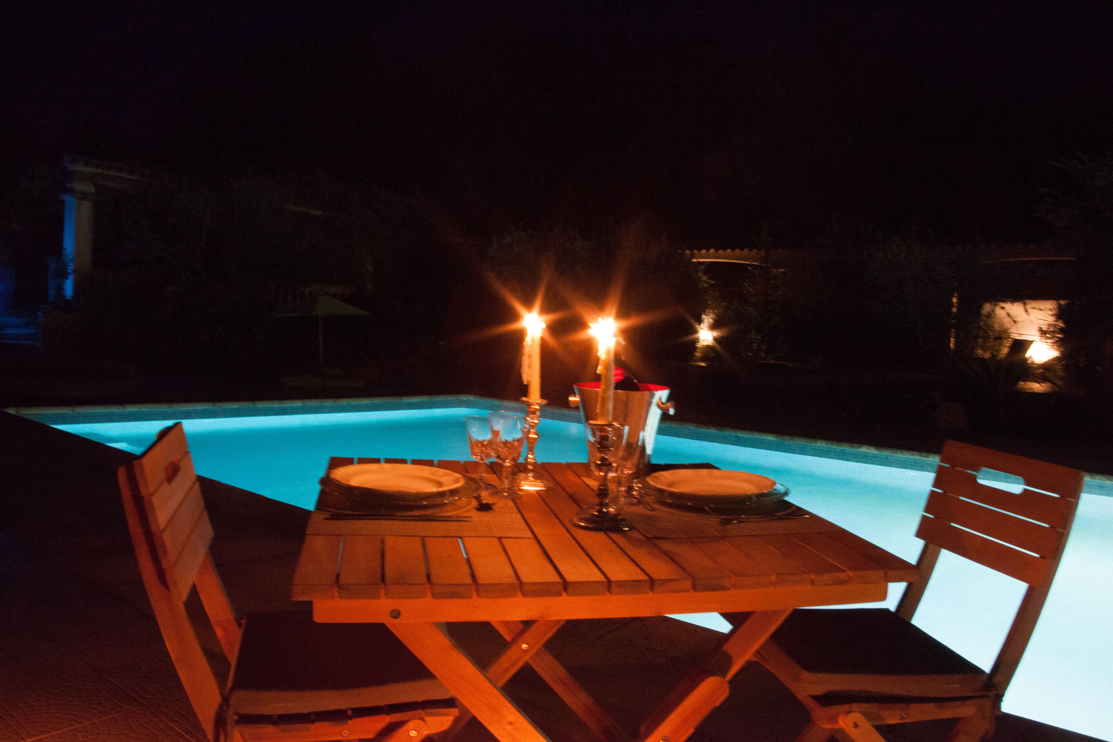 Tavolo da pranzo imbandito per due, con candele, vicino a una piscina di notte.