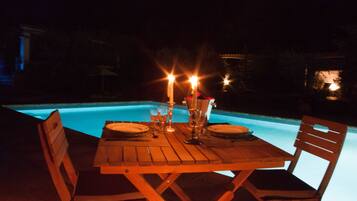 Tavolo da pranzo imbandito per due, con candele, vicino a una piscina di notte.