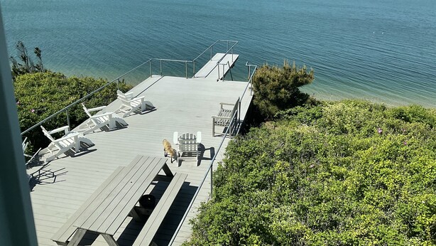 Une terrasse en bois avec des sièges extérieurs, donnant sur une étendue d’eau.