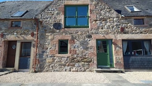 Un bâtiment en pierre doté d’une fenêtre centrale, d’une porte verte et d’une petite fenêtre circulaire située au-dessus de la porte.