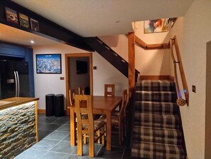 A dining area with a wooden table and chairs, a stone accent wall, and a staircase with a plaid blanket. - Swordale Stays. Self catering holiday cottage in the Highlands of Scotland. (Dingwall)
