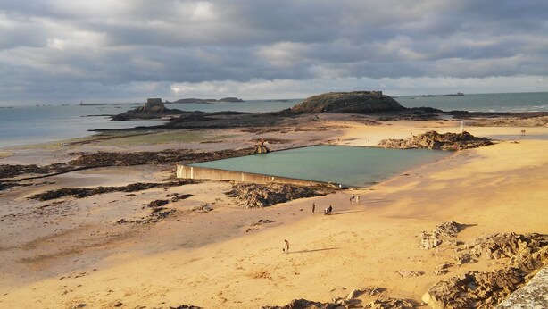 A beach with a large pool, rocky terrain, and a distant island.
