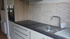 A modern kitchen with white cabinets, a black countertop, a stainless steel sink, and a built-in oven.
