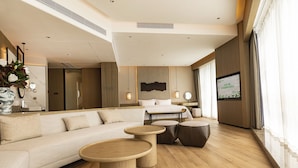 A modern hotel room with a sofa, two round wooden tables, a bed, and a TV on the wall. - Wyndham Garden Gaozhou (Maoming)