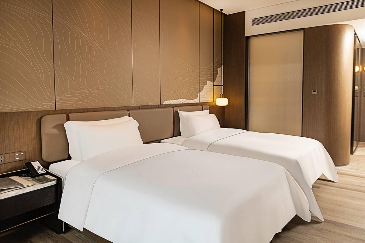 Une chambre d’hôtel avec deux lits, une table de chevet, une lampe et une armoire.