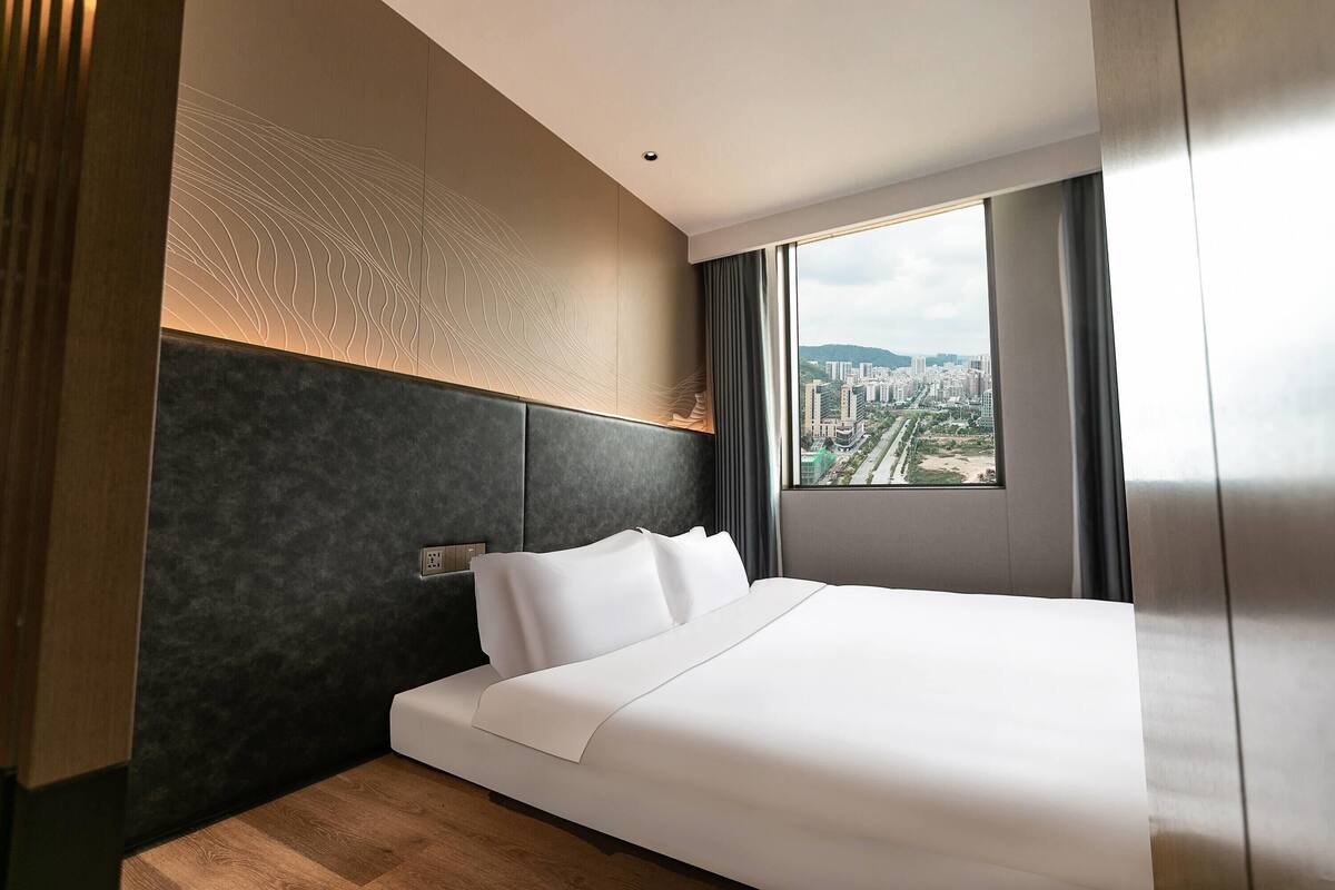 Une chambre d’hôtel moderne dotée d’un grand lit, offrant une vue sur la ville et présentant un décor mural original.