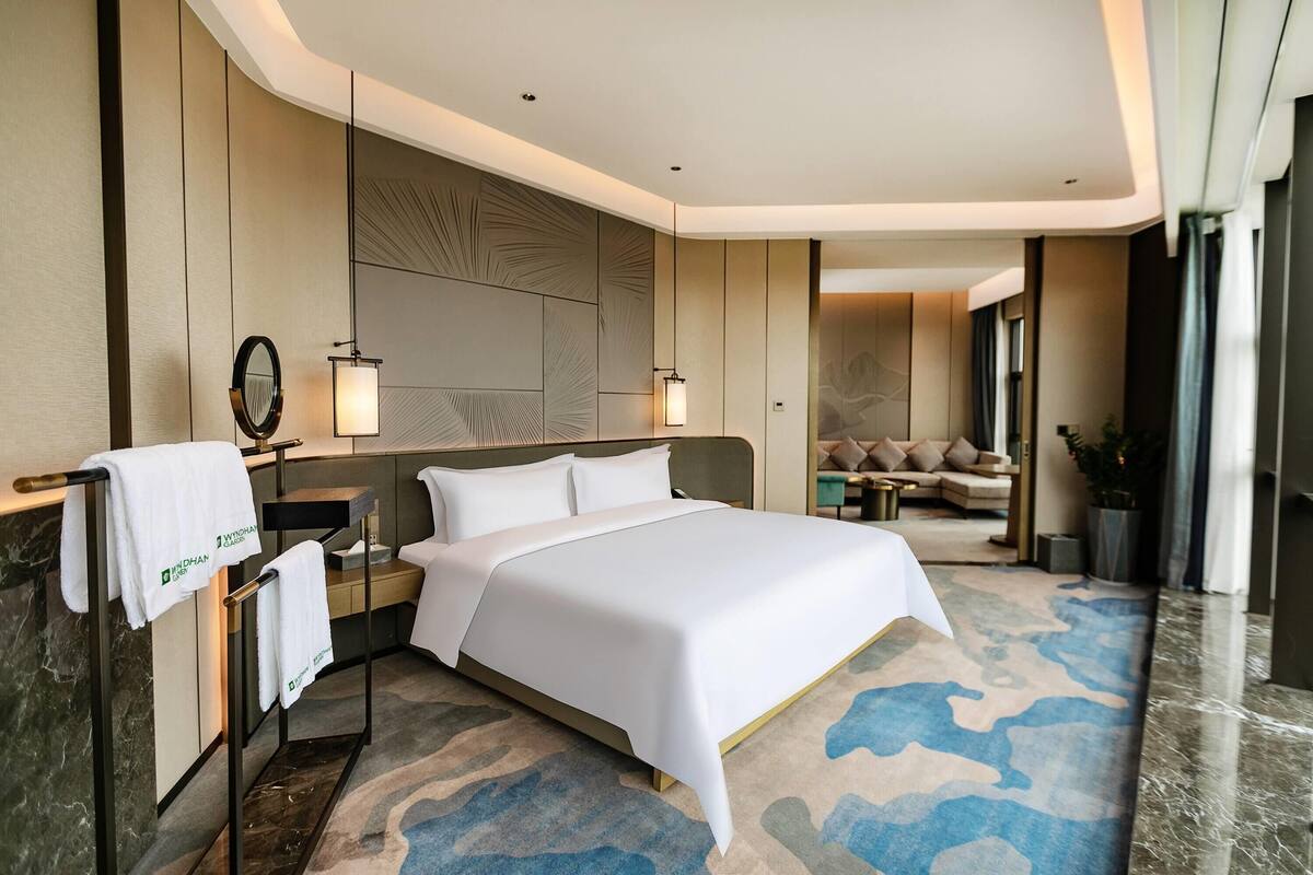 Une chambre d’hôtel moderne dotée d’un grand lit, d’une table de chevet, d’un miroir et d’un coin salon avec un canapé et une petite table.