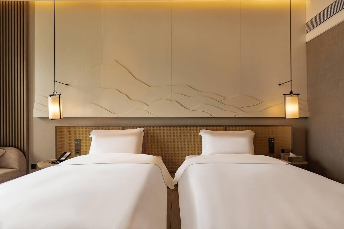 Une chambre d’hôtel avec deux lits, une table de chevet avec un téléphone et un luminaire fixé au mur.