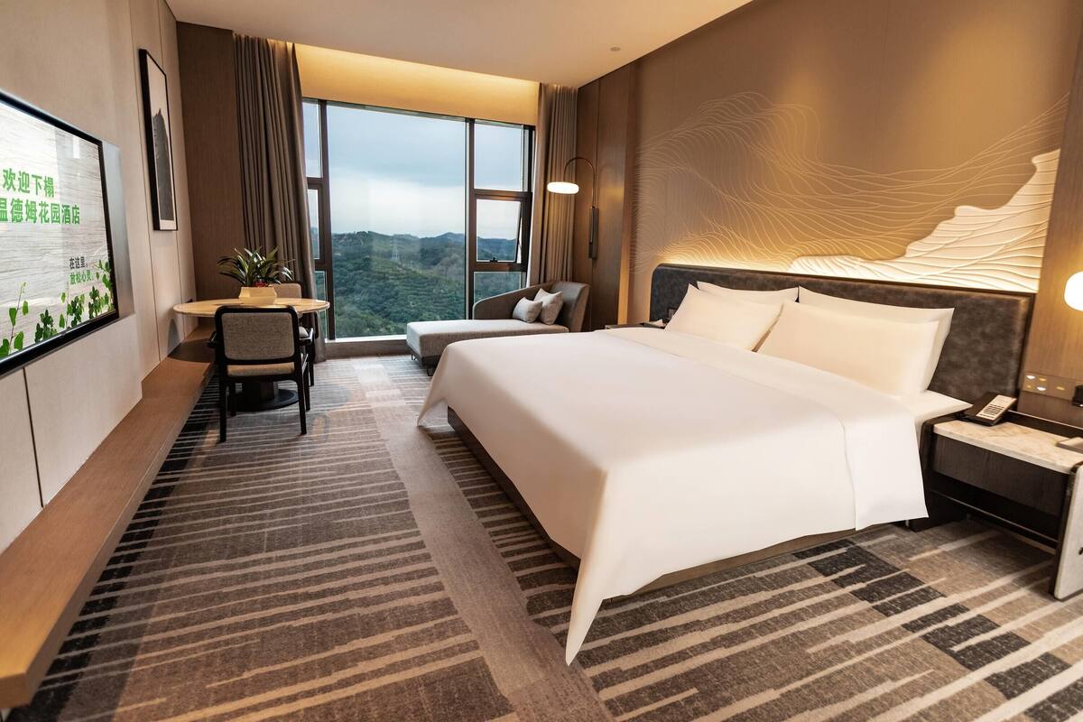 Une chambre d’hôtel avec un grand lit, un bureau avec une chaise, une télévision et une vue sur les montagnes.