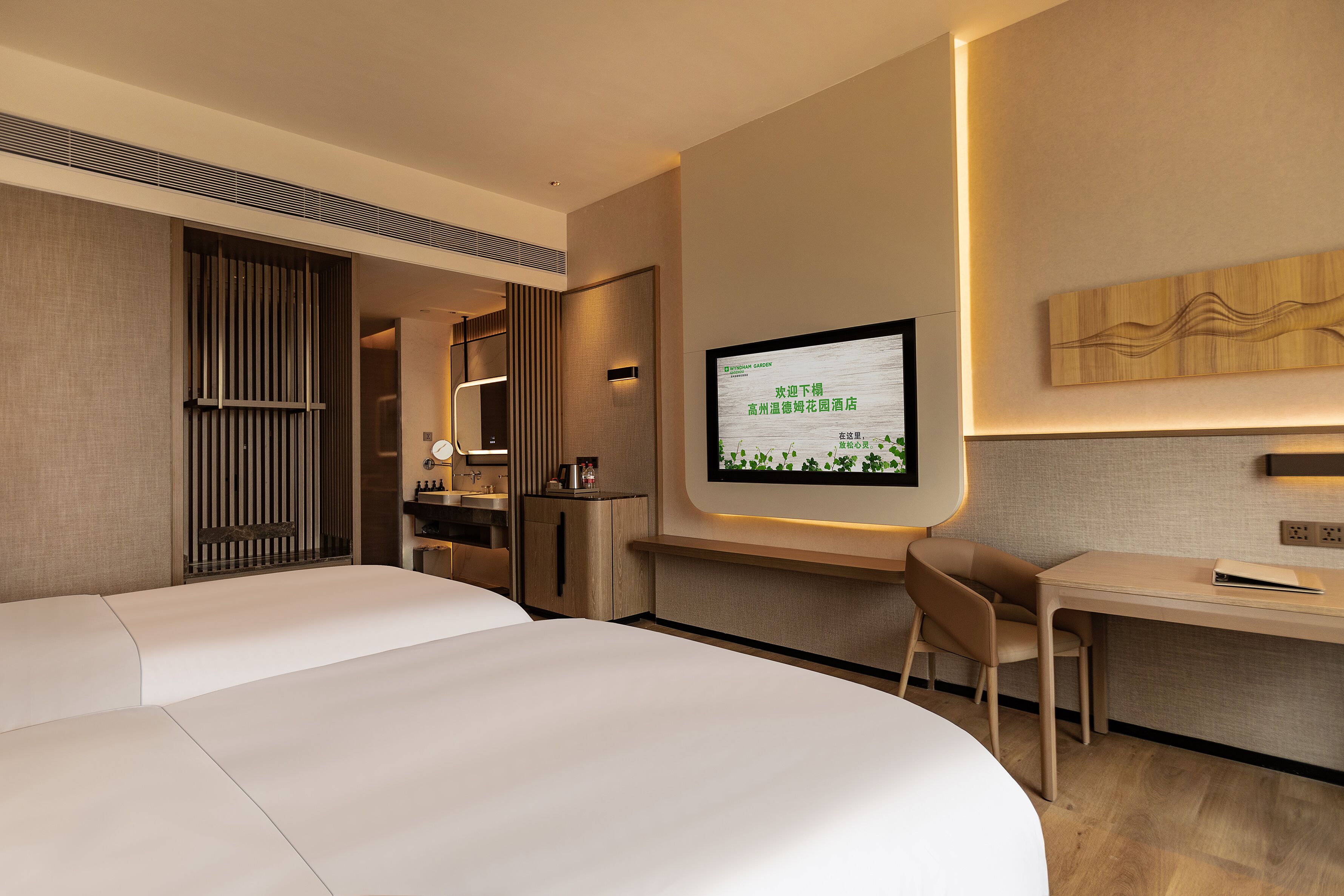 A modern hotel room with a large bed, a desk, a chair, and a television mounted on the wall.
