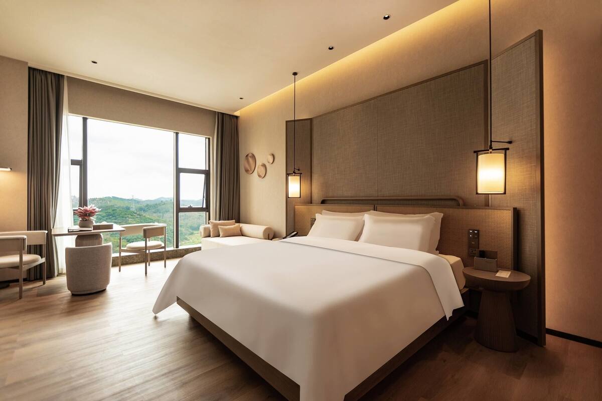 Une chambre d’hôtel moderne, dotée d’un grand lit, d’un bureau et offrant une vue sur l’extérieur.