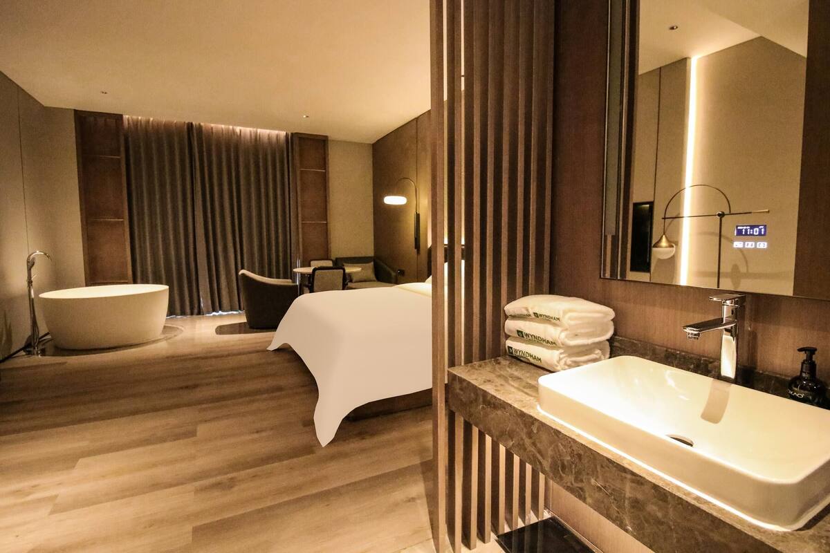 Une chambre d’hôtel moderne dotée d’une grande baignoire, d’un coin salon séparé et d’une coiffeuse avec un lavabo.