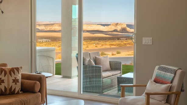 A room with a large sliding glass door leading to a balcony with a view of a desert landscape. There are two sofas and a chair inside the room. - Pueblo en Powell - Hot Tub, Game Room, Lake Views (Page)