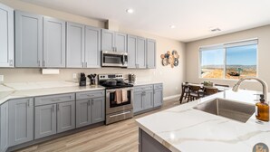 A modern kitchen with grey cabinets, a stainless steel stove, and a large window offering a desert view. - Pueblo en Powell - Hot Tub, Game Room, Lake Views (Page)