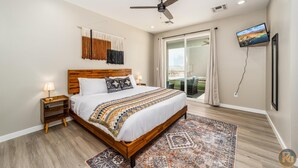A bedroom with a wooden bed, a ceiling fan, a TV, and a large window with curtains. - Pueblo en Powell - Hot Tub, Game Room, Lake Views (Page)