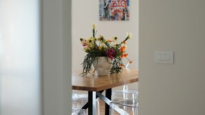 Een eethoek met een houten tafel, een witte vaas met bloemen en een muur met een poster.
