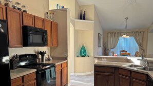 A kitchen with wooden cabinets, a black stove, a microwave, and a sink. - Magic Sunset (Kissimmee)