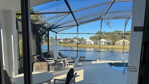 A covered patio with outdoor furniture, a pool, and a view of a lake and houses in the background. - Magic Sunset (Kissimmee)