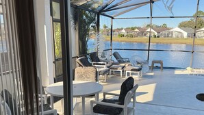 A covered outdoor seating area with chairs and tables, overlooking a body of water and houses in the background. - Magic Sunset (Kissimmee)