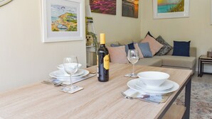 A dining table set with wine glasses, a bottle, and plates, with a sofa and cushions in the background. - 1 bedroom accommodation in Wellow, near Yarmouth (Wellow, near Yarmouth)