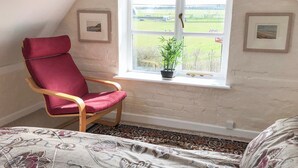 A room with a red chair, a window with a view of a field, and a bed with patterned bedding. - 1 bedroom accommodation in Wellow, near Yarmouth (Wellow, near Yarmouth)