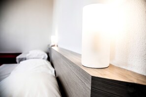 Una cama con ropa blanca y una mesita de noche con una lámpara blanca.