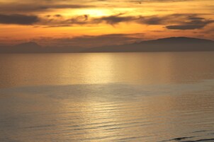 Mar calmo ao pôr do sol, com silhueta de montanhas ao fundo.