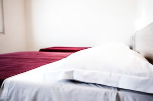 Una cama con ropa de cama blanca y roja, una pared lisa y una ventana al fondo.