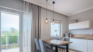 A modern kitchen with a dining area, large windows, and a view of greenery.