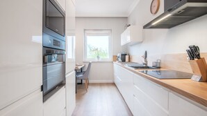 A modern kitchen with white cabinets, a built-in oven, a coffee machine, and a window with a view of greenery.