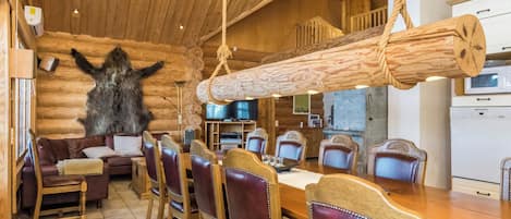Ein Interieur einer Blockhütte mit Essbereich, Holzmöbeln und einem großen Felltiermotiv an der Wand.