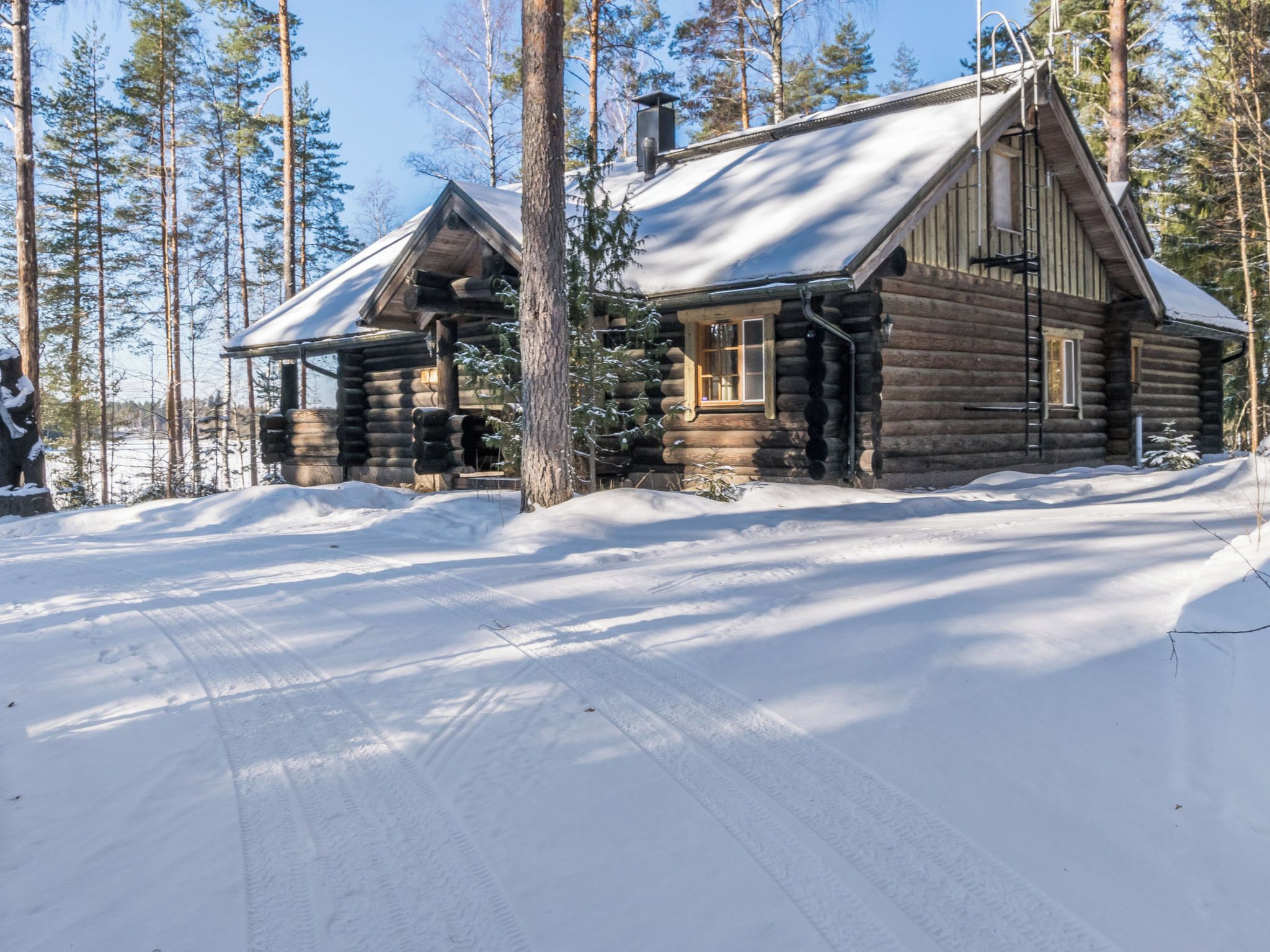 A log cabin with a snow-covered roof, surrounded by a forest.