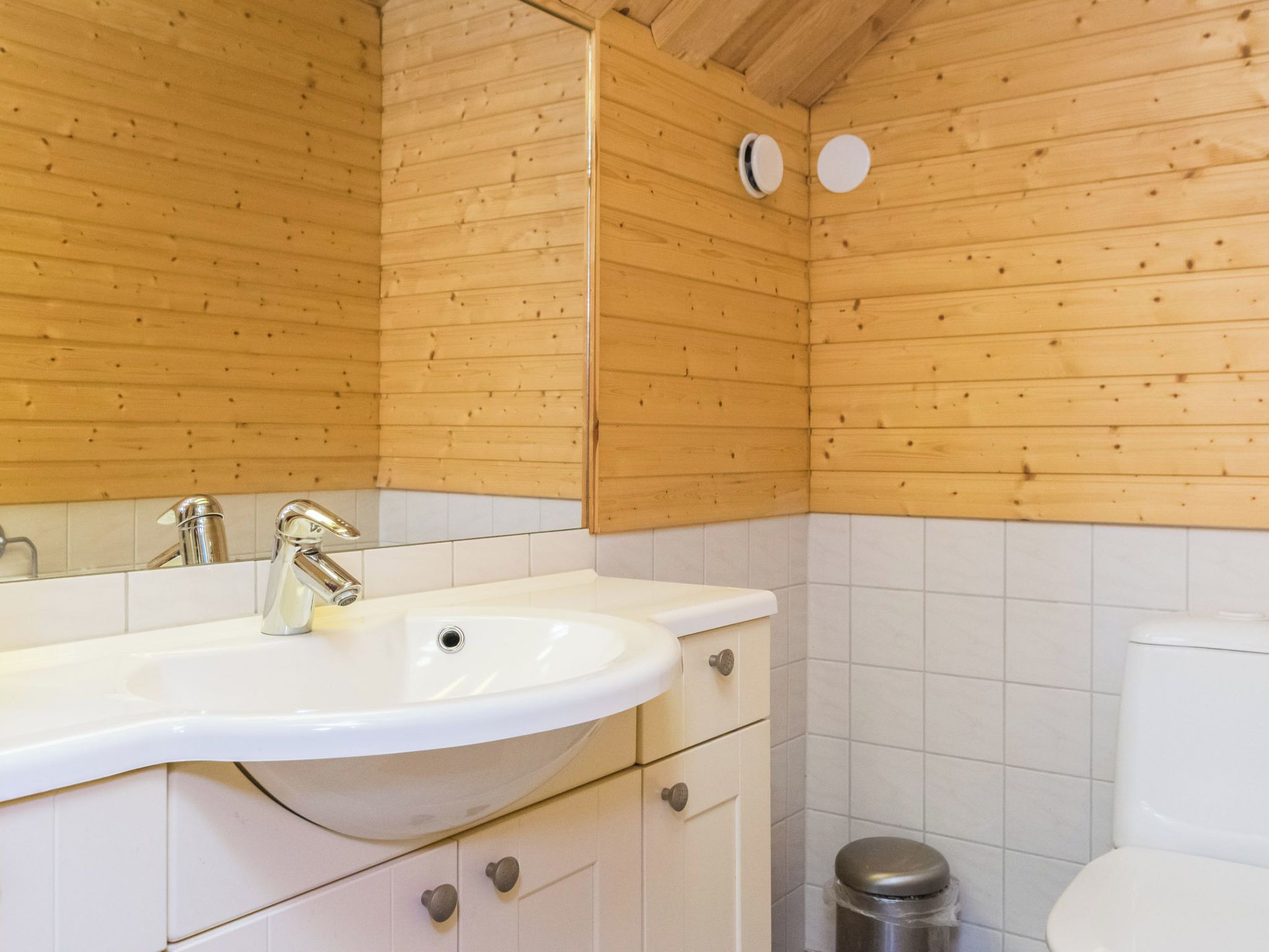Un bagno con pareti in legno, un lavandino bianco, uno specchio e un water.