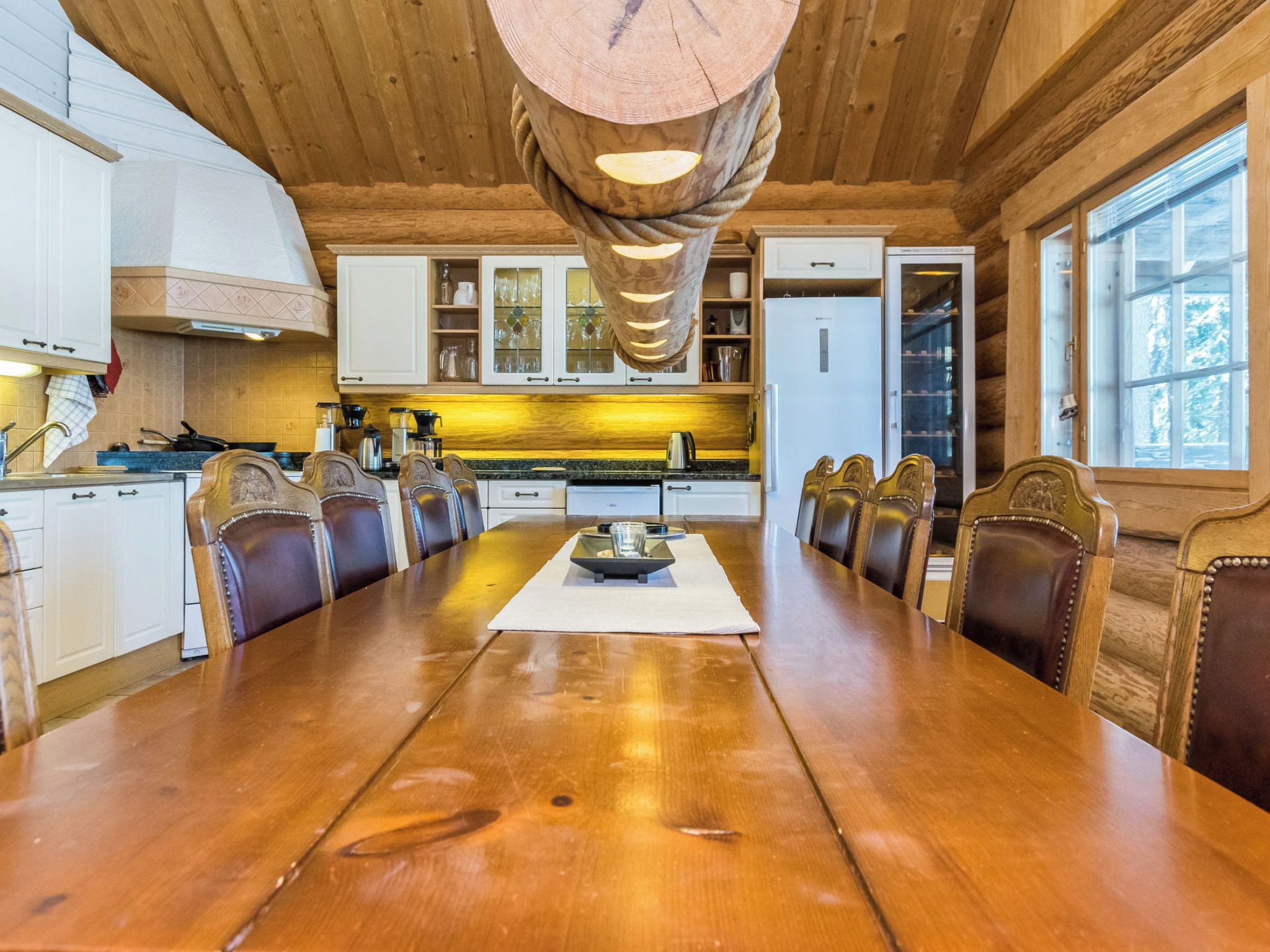Eine geräumige Küche mit einem langen Holztisch, weißen Schränken und einem modernen Kühlschrank.