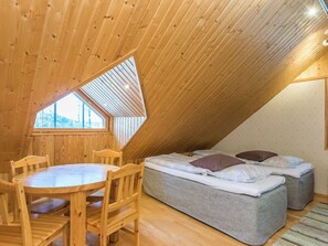Une chambre confortable située dans les combles, avec un plafond en pente en bois, une petite fenêtre, un lit avec des oreillers et une table à manger en bois, accompagnée de chaises.