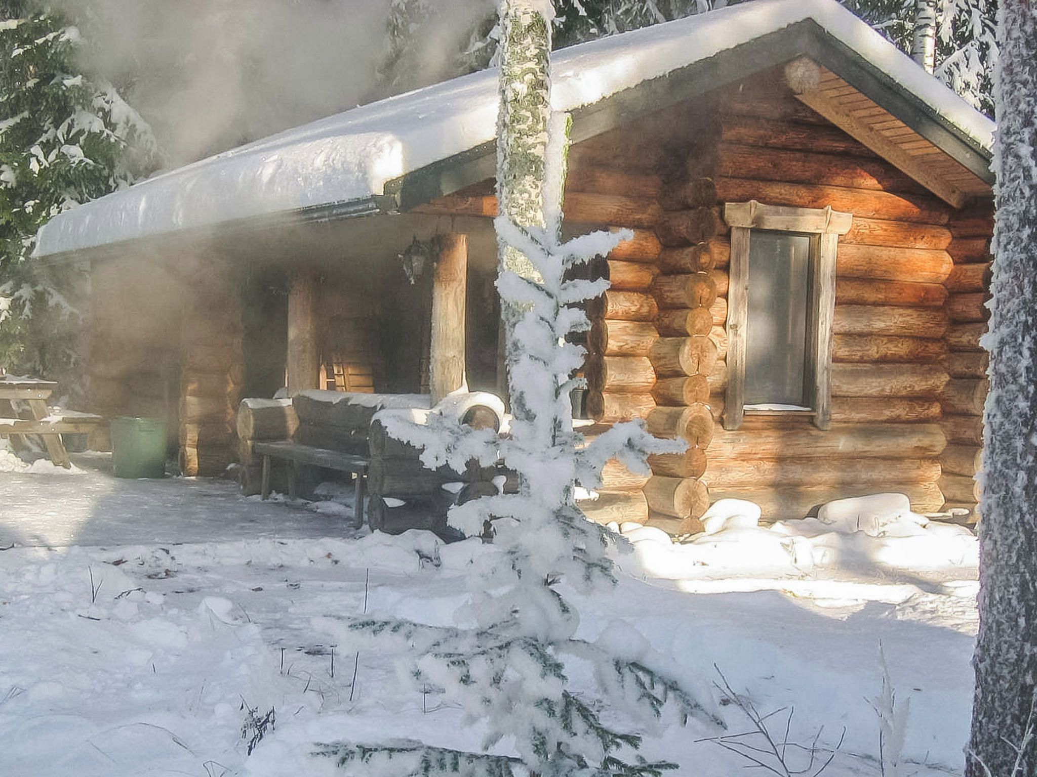 Una cabaña de troncos con un porche y una chimenea que expulsa humo.
