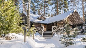 Una cabaña de troncos con techo nevado y fachada de madera, rodeada de altos pinos.