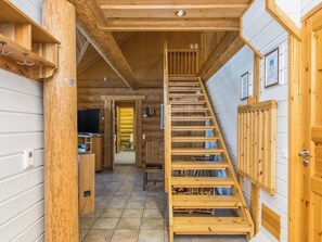 Un intérieur en bois avec un escalier menant à une mezzanine, une cuisine équipée d’un évier et de placards, et une porte dotée d’une poignée.