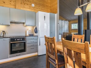 A modern kitchen with a built-in oven, a refrigerator, and a dining area with wooden chairs.