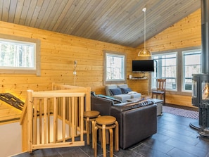 Ein Holzblockhaus-Innenraum mit Wohnbereich, einem Fernseher, einem Kamin und einem Babybett.