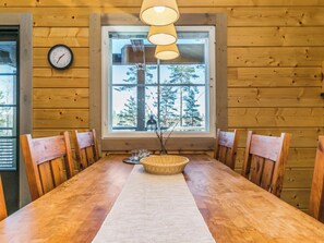 A wooden-paneled room with a dining table, chairs, a clock, and a window with a view of trees.