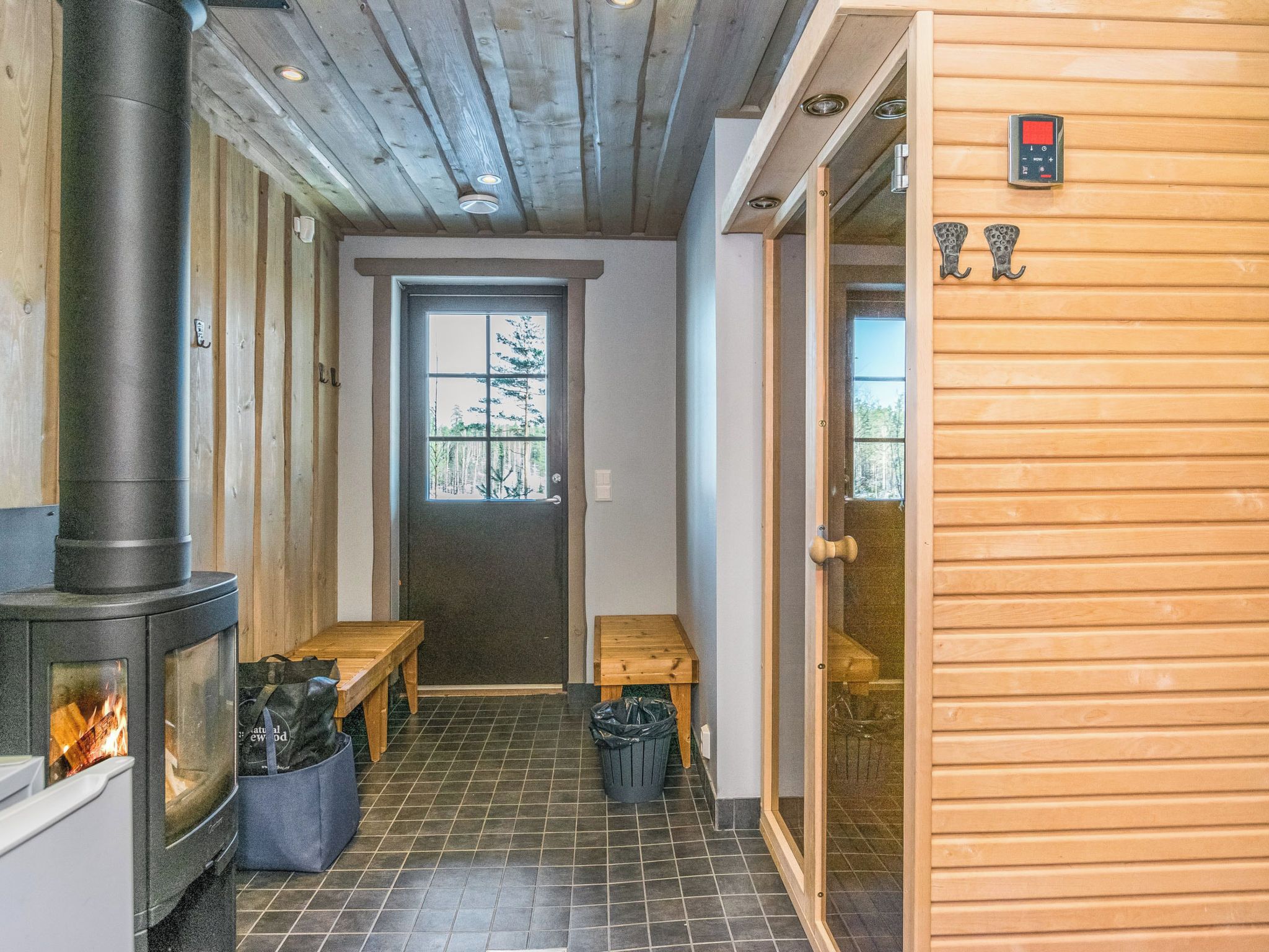 A room with a wood-burning stove, a bench, a door, and a window.