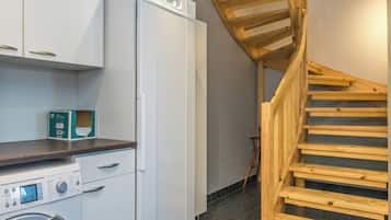 A compact kitchen with a washing machine, a refrigerator, and a wooden staircase.