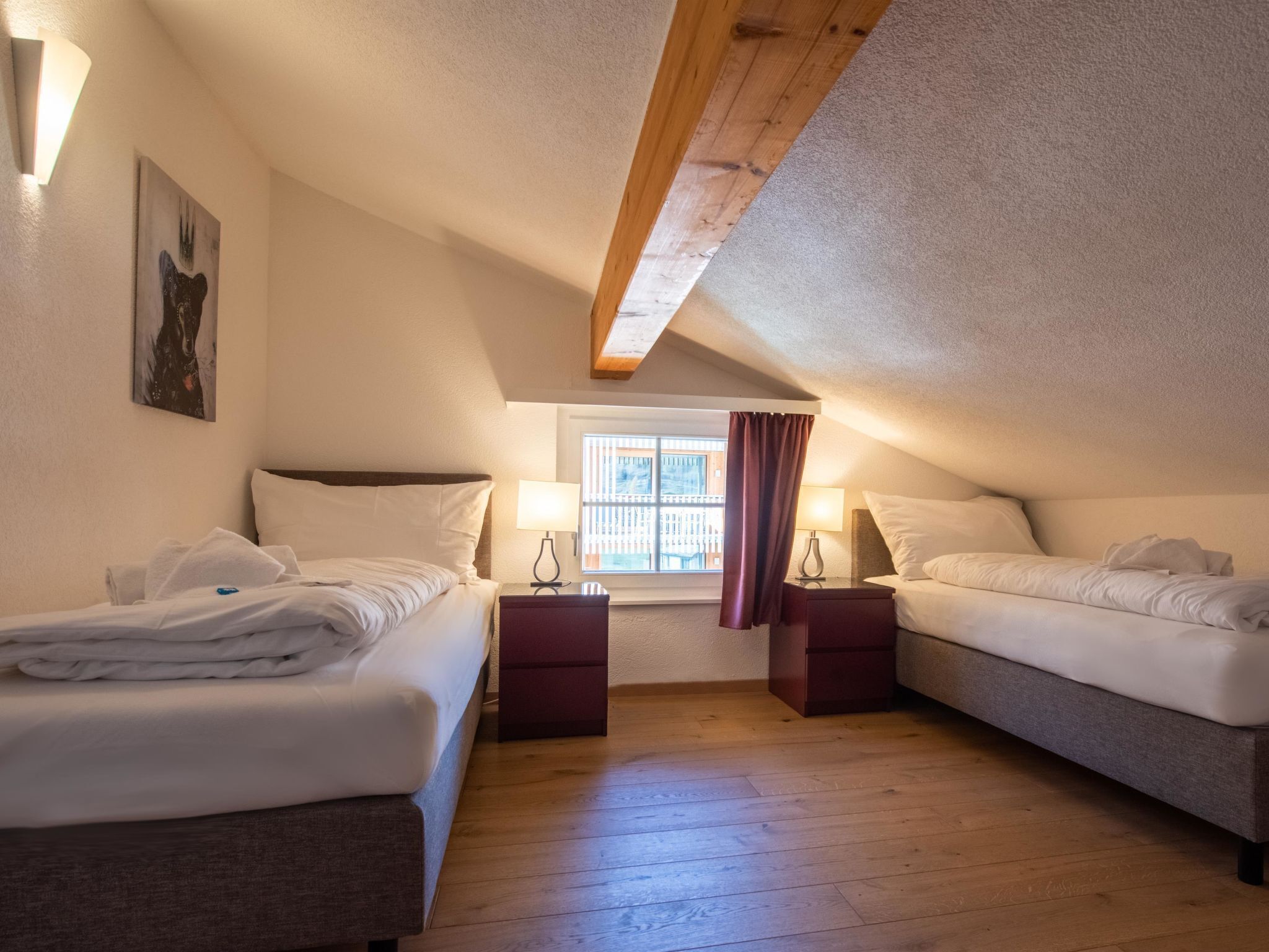 Une chambre confortable située sous les combles, avec deux lits, une fenêtre avec des rideaux et un plafond en bois.